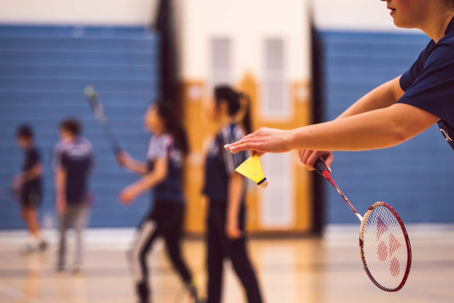 Joueuse de badminton tend un volant jaune au-dessus d'un gymnase, raquette en main
